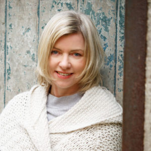 danielle mclaughlin smiles with short blonde hair and white knitted sweater