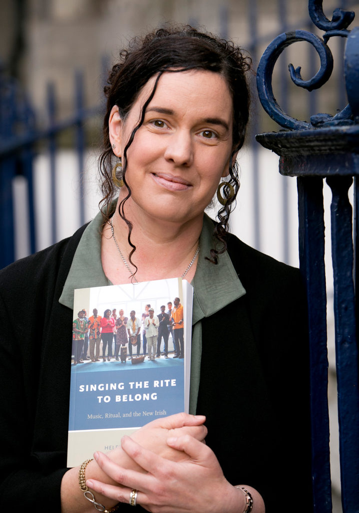 helen phelan stands by wrought iron fence holding a book