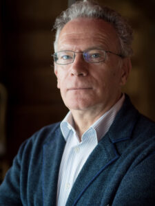 Fintan O'Toole gazes at the camera. He wears glasses, has greying hair, and wears a white collar shirt under navy blazer.