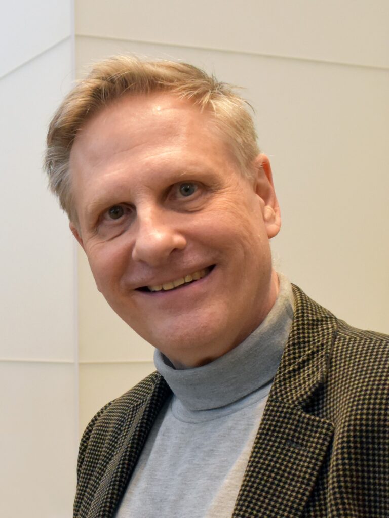 Robert Spoo smiles, wearing a grey turtleneck and brown blazer